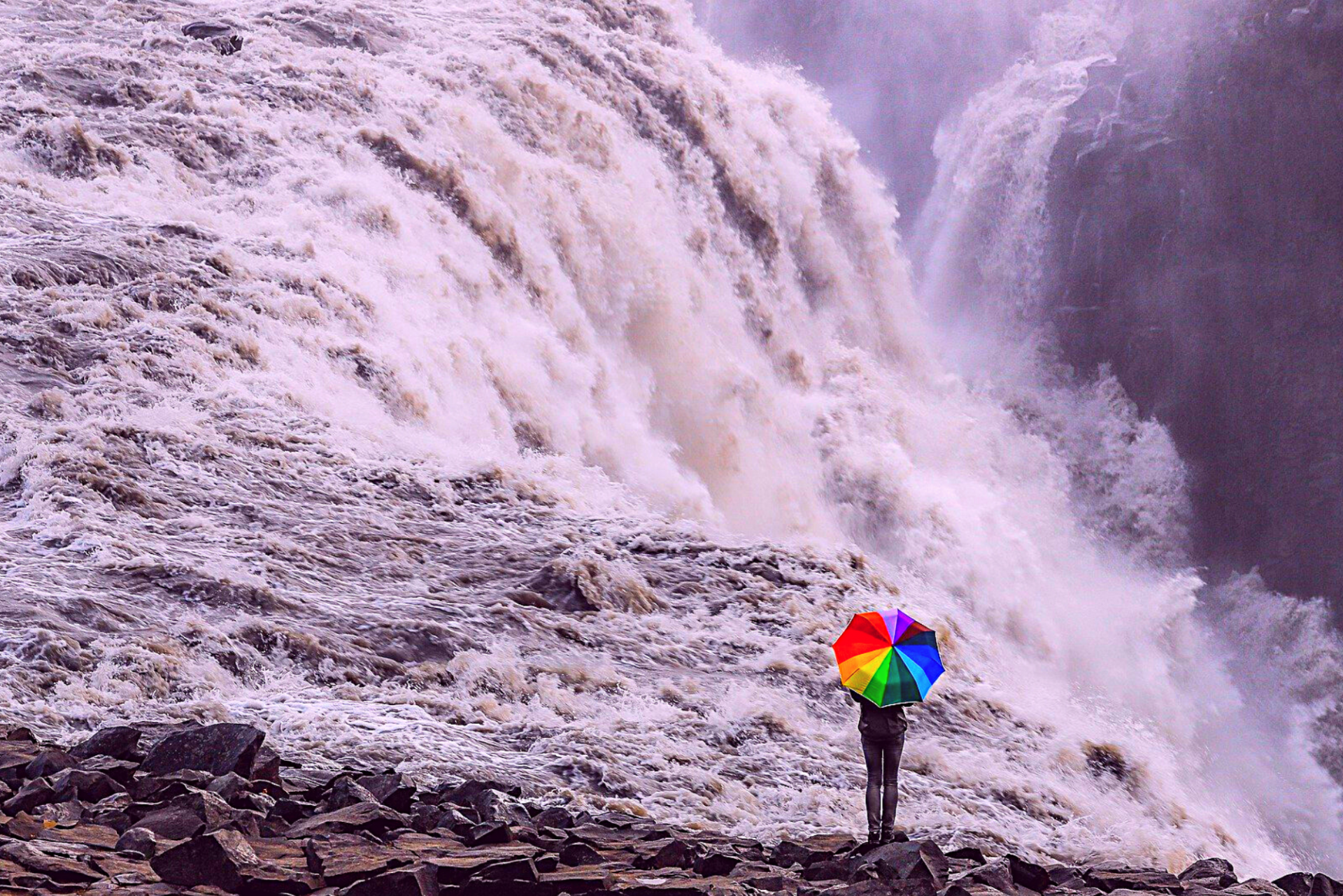 person with a colourful umbrella standing over a waterfall
